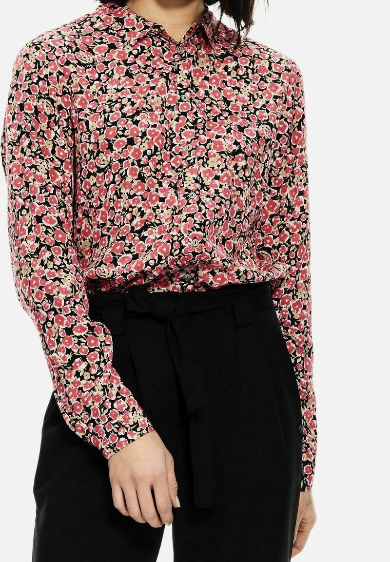 Floral button-up shirt in pink and black with small flower patterns, long sleeves, and a pointed collar, paired with black trousers.