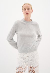 Pulover texturat, de culoare gri deschis, cu guler rotund și mâneci lungi, are un tiv inferior ajustat. Este purtat cu pantaloni scurți din dantelă alba.