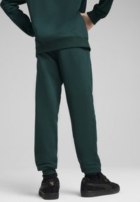 Ciemnozielone bawełniane spodnie dresowe o tapered designie, z elastycznym pasem i ściągaczami, w połączeniu z czarnymi sneakersami.
