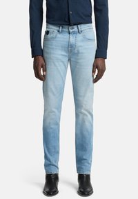 Jeans in denim azzurro chiaro con vestibilità slim, caratterizzati da dettagli scoloriti e design a cinque tasche. Abbinati a stivaletti neri alla caviglia e una camicia blu navy.