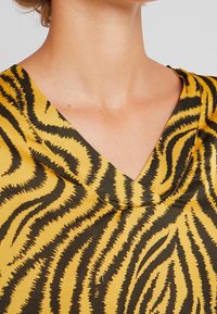 Primo piano di una persona che indossa una maglietta a V gialla e nera a strisce tigre, che mostra il neckline e la parte superiore del petto.