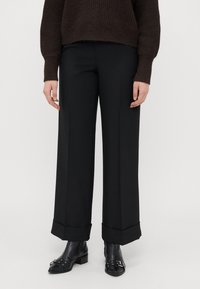 Wide-leg black trousers with a tailored fit, featuring a smooth texture and turned-up cuffs, paired with black ankle boots.