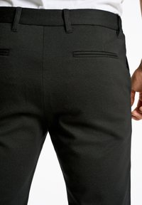 Sorte skræddersyede bukser lavet af tekstureret stof, med to baglommer med diskret syning og et lige ben design.
