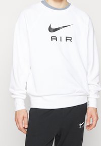 Vit sweatshirt med rund halsringning, grå detaljer på kragen, stor svart "AIR" logotyp på framsidan samt ribbade manschetter och fåll.