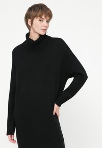Crna pletena turtleneck pulover, oversized dizajn, rebrasti manžeti i donji rub, s opuštenim siluetom i teksturiranom tkaninom.