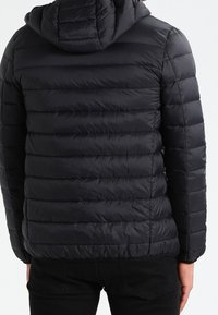 Schwarze Steppjacke mit Kapuze, die ein gestepptes Design, horizontale Nähte und eine glatte, glänzende Textur aufweist. Geeignet für kaltes Wetter.