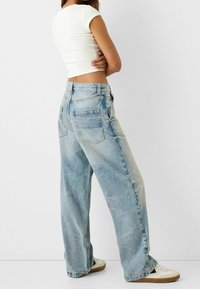 Lichtblauwe wijde jeans met een vervaagde wassing, featuring achterzakken en een hoge taille. Gecombineerd met witte schoenen en een getailleerd wit shirt.