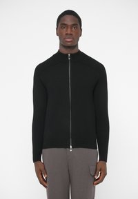 Čierny zapínací sveter so zipsom, rebrovanou textúrou, vysokým golierom a dlhými rukávmi; hladká látka s kovovými detailmi na zips a priliehavým strihom.
