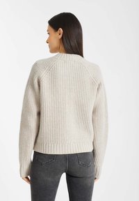 Licht beige geribbelde trui met een ronde halslijn, brede manchetten en een zoom net boven de heupen, gecombineerd met donkergrijze jeans.