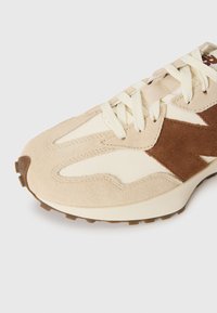 Prim-plan al sneakerilor din suede bej și maro, cu sireturi cremoase și talpă de cauciuc texturată.