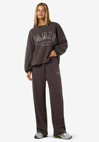 Tummanruskeat collegehousut ja niihin sopiva collegepaita, jossa lukee "PARIS" valkoisella tekstillä. Pehmeä kangas, rento leikkaus ja joustava vyötärö.