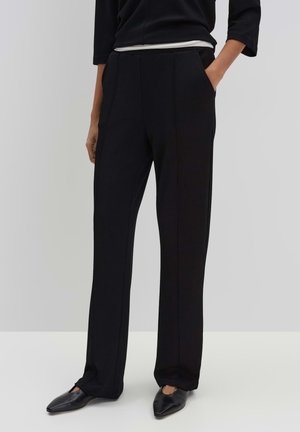Zwarte op maat gemaakte broek met een recht model, voorzien van zijzakken en een gladde textuur, gecombineerd met spitse zwarte schoenen.
