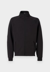 Sweat-shirt noir zippé avec col montant, poignets côtelés et poche devant. Présente un petit logo noir sur la poitrine. Texture lisse.