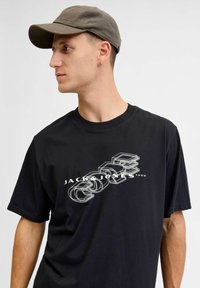 Must mõõdud must puuvillane T-särk, millel on valge graafiline trükk brändi nime "Jack & Jones" modernses disainis. Komplekti kuulub tumedat värvi müts.