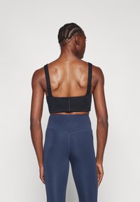 Μαύρο αθλητικό σουτιέν με φαρδιές τιράντες και λεία υφή, που διαθέτει εφαρμοστή σχεδίαση. Συνδυασμένο με ναυτικά κολάν ψηλής μέσης.