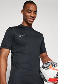T-shirt de sport noir à manches courtes, arborant un logo Nike blanc sur la poitrine gauche. Le t-shirt a un design lisse et ajusté.