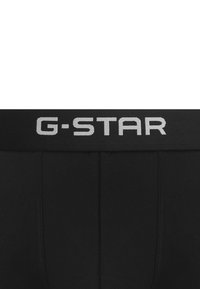 Boxers noirs G-Star avec une large ceinture élastique portant le logo "G-STAR" en gris. Tissu lisse, coupe ajustée, sans motifs supplémentaires.