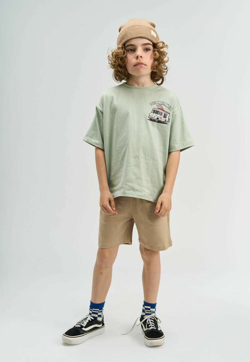 Tamnoplavi T-shirt kratkih rukava u boji mente s grafikom kamiona sladoleda, uparen s bež šortsem i crnim tenisicama uz plave i bijele prugaste čarape.