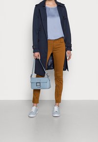 Cappotto trench navy, blusa di satin azzurro chiaro, pantaloni skinny senape, borsa azzurra chiara e sneakers azzurre chiare con lacci bianchi.
