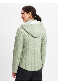 Grüne gesteppte Jacke mit Kapuze und weißen Akzenten. Strukturiertes Material, taillierte Passform und gerader Saum hinten.