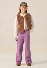 Gilet en polaire marron avec des motifs en forme de cœur violets, chemise blanche à boutons, et pantalon large lavande. Le porteur porte une casquette à imprimé léopard.