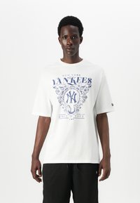 Balta medvilnė marškinėliai su m�ėlyna New York Yankees grafika, trumpomis rankovėmis, laisvo pjūvio ir apvali iškirpte. Tekstas apima "nuo 1903".