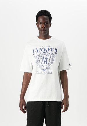 Fehér pamut póló kék New York Yankees grafikai dizájnnal, rövid ujjú, laza szabású és kerek nyakkivágású. A szöveg tartalmazza: "1903 óta".