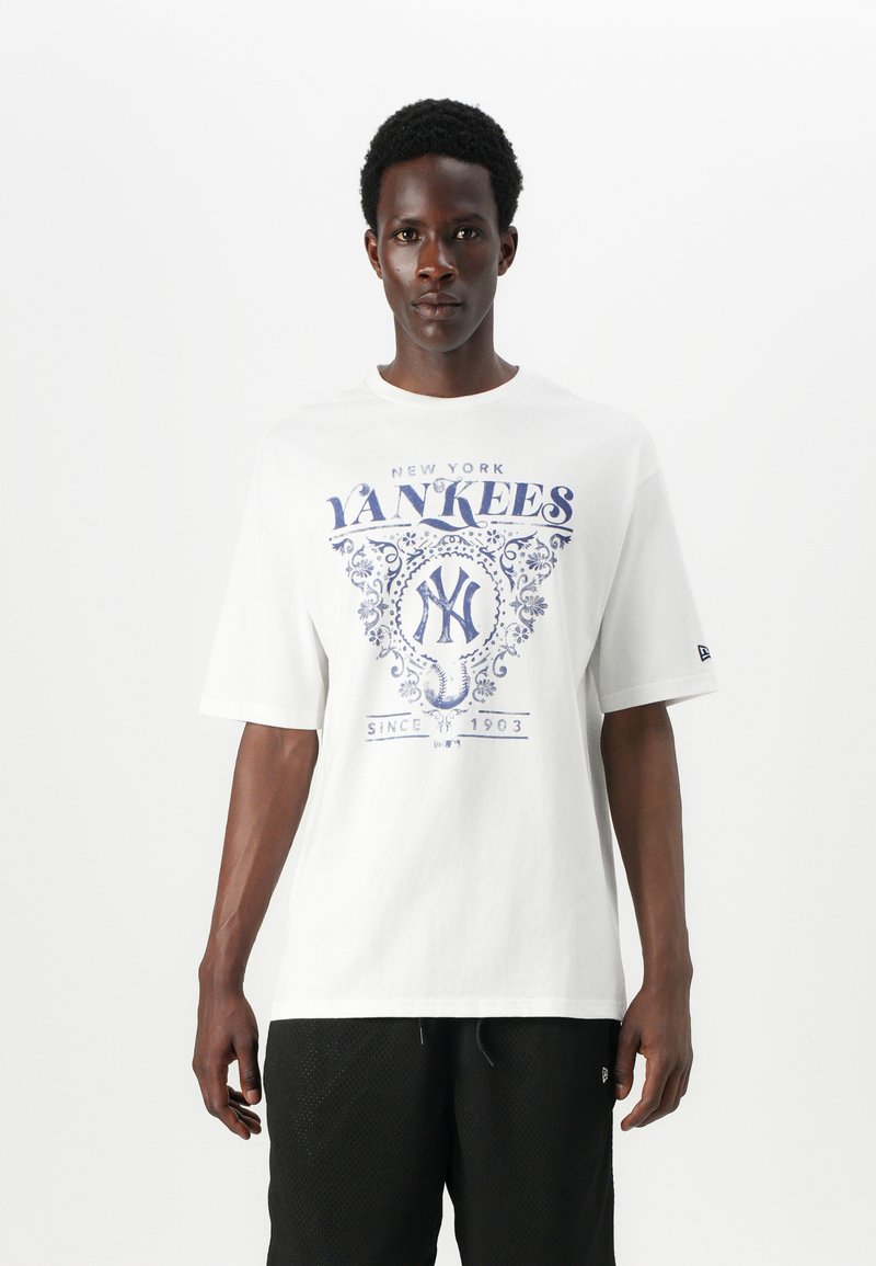 Balta medvilnė marškinėliai su mėlyna New York Yankees grafika, trumpomis rankovėmis, laisvo pjūvio ir apvali iškirpte. Tekstas apima "nuo 1903".