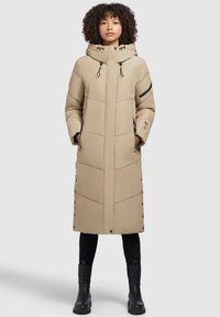 Beige langer Puffermantel mit Kapuze, mit gesteppten Mustern, seitlichen Taschen mit Reißverschlüssen und Druckknopfverschlüssen auf der Vorderseite. Schwarze Akzentdetails.