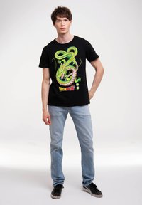 Camiseta de algodón negra con un gráfico colorido de un dragón de Dragon Ball Z, con acentos en verde y amarillo, combinada con jeans de color azul claro.