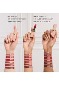 Drie handen met verschillende huidtinten tonen lippenstiftbuisjes en kleurstaaltjes van zes tinten met de volgende labels: 601 Worth It, 570 Worth It Intense, 300 Rouge Paris, 560 Rosewood, 545 Nude Nonchalant en 580 Brun Elegance.