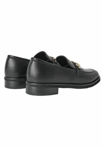Scarpe slip-on in pelle nera con punta rotonda, tacco basso e hardware decorativo dorato sulla parte anteriore. Finitura liscia con minima texture.
