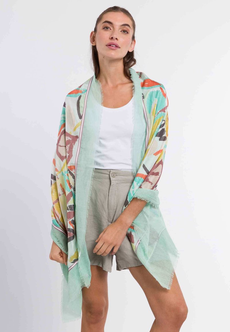 Sciarpa leggera e semitrasparente di colore verde menta con motivi astratti multicolori. I bordi sono sfrangiati. Adatta per essere indossata in sovrapposizione.
