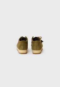 Zapatos de ante verde oliva con un acabado texturizado, que cuentan con una suela de goma y un detalle en bucle en el talón. La vista trasera muestra líneas de diseño limpias.