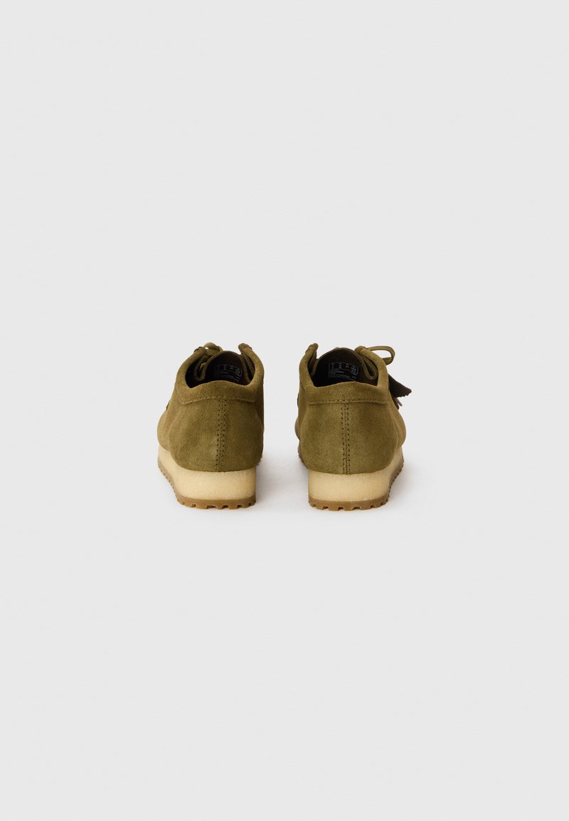 Zapatos de ante verde oliva con un acabado texturizado, que cuentan con una suela de goma y un detalle en bucle en el talón. La vista trasera muestra líneas de diseño limpias.