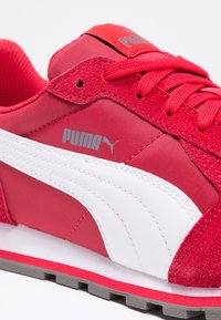 Baskets Puma rouge et blanc, dotées d'un mélange de daim texturé et de matériaux synthétiques lisses, avec une semelle en caoutchouc et un design classique.