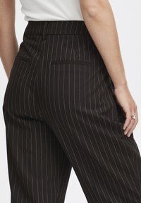 Zwarte broek met streepdessin heeft een getailleerde pasvorm, een platte voorkant, twee achterzakken en een soepele stoftextuur.