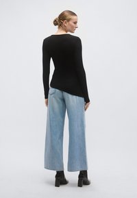 Bluză neagră cu mâneci lungi asortată cu blugi largi de culoare albastru deschis, având o textură netedă și cusături subtile ca accente. Încălțăminte cu toc negru completează ținuta.