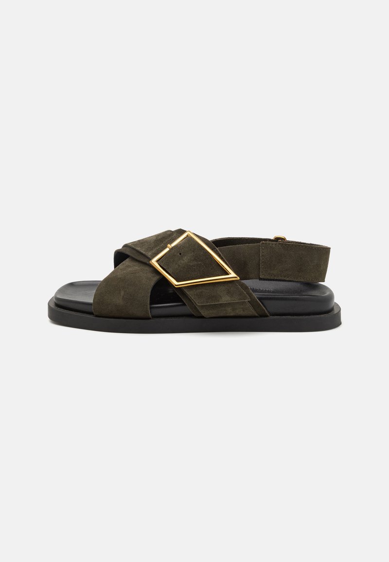 Green suede sandal with crossover straps, black rubber sole, and a gold rectangular buckle accent. Back strap for secure fit.