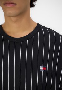 Svartstripete t-skjorte med hvite vertikale linjer, med rund hals og en liten Tommy Jeans-logo på brystet.