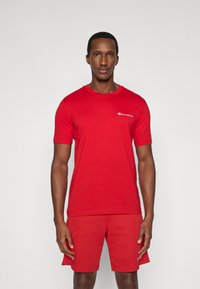 Κόκκινη βαμβακερή μπλούζα με στρογγυλή λαιμόκοψη, κοντά μανίκια και ένα μικρό λευκό λογότυπο στο αριστερό μέρος του στήθους. Συνδυασμένη με αντίστοιχα κόκκινα σορτς.