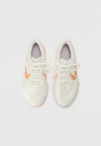Zapatillas blancas ligeras con superficie texturizada, swoosh naranja de Nike y detalles en lavanda. Cuentan con cordones planos y lengüeta acolchada.