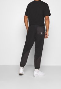 Svart T-shirt med korta ärmar, tillsammans med mörkgrå sweatpants med triangulära detaljer och en bakficka. Vita sneakers.