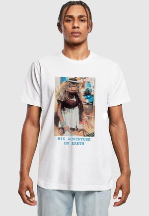 White t-shirt with a colorful graphic of a puppet in a dress and hat, featuring the text "HIS ADVENTURE ON EARTH" in blue.