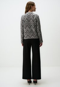Grau gemusterter Pullover mit einem Zickzack-Design, kombiniert mit schwarzen weit geschnittenen Hosen und schwarzen Absätzen. Die Textur wirkt weich und gestrickt.