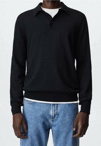 Polo à manches longues noir avec col et fermeture à boutons, présentant un ourlet ajusté et une texture douce et lisse. Porté avec un denim bleu clair.