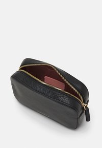 Černé kožené pouzdro s texturovaným povrchem, zlatým kovovým zipem a tmavě červeným vnitřkem. Uvnitř má štítek s logem. Kompaktní a obdélníkový tvar.