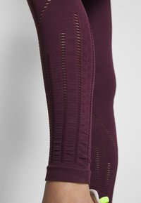 Burgundské legíny na cvičení s texturovanými panely a vertikálními výřezy, hladký materiál a přiléhavý střih se zakončením na manžety.