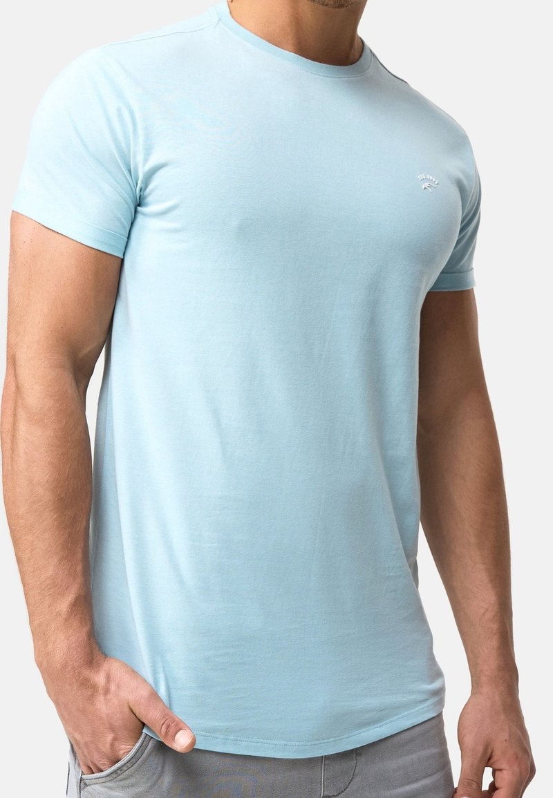 T-shirt bleu clair à manches courtes en tissu doux, avec un col rond et un petit logo sur la poitrine.