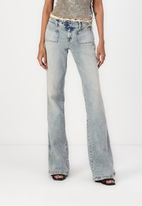 Vaqueros acampanados de color azul claro con un lavado desvanecido, que cuentan con dos bolsillos frontales y un cierre de cremallera con botón. Combinados con una blusa ajustada y tacones.